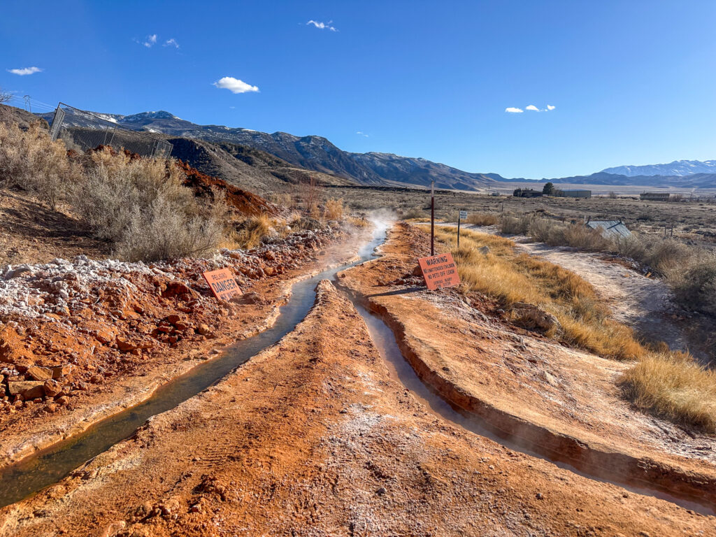 A desert landscape with a y-shaped stream of hot spring water running through the red sandstone, with a blue sky.