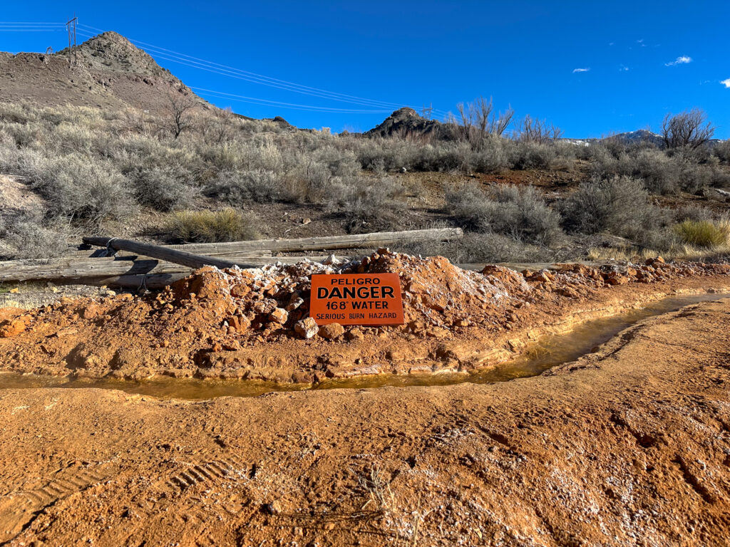 A hot spring running over sandstone with an orange sign reading:  "Peligro, Danger, 168º Water, Serious Burn Hazard" in black capital text.