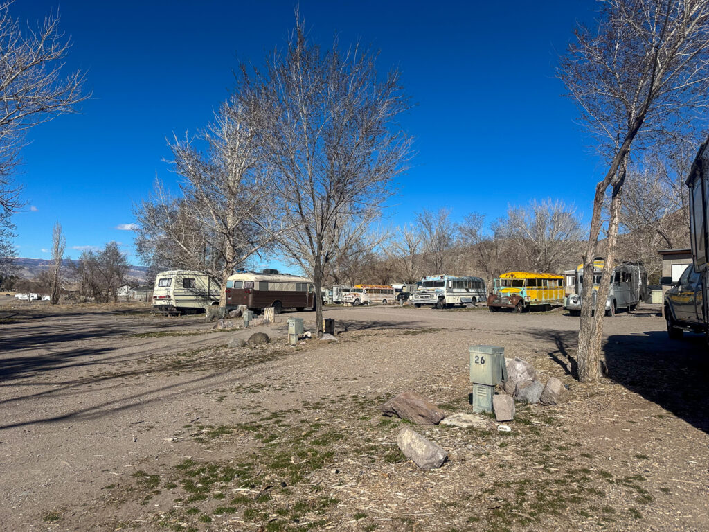 RV hookup sites with gravel driveways and vintage buses in the background at Mystic Hot Springs in Monroe, Utah.